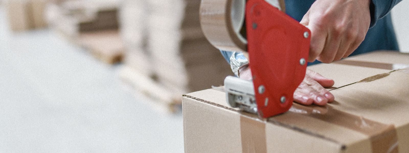 Nahaufnahme von Händen, die einen Versandkarton mit einem Handabroller und braunem Klebeband professionell verschließen